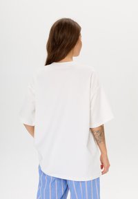 Witte oversized T-shirt met korte mouwen, voorzien van een ronde halslijn, een gladde textuur en een ontspannen pasvorm, gecombineerd met blauwgestreepte broek.