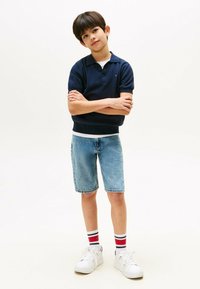 Granatowa koszulka polo z krótkim rękawem, jasnoniebieskie szorty dżinsowe i białe sneakersy w czerwono-niebieskie paski. Prosta, codzienna stylizacja.