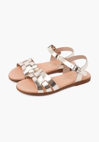 Sandali metallici dorati con suola piatta, caratterizzati da cinturini incrociati e chiusura con fibbia. Suola interna morbida con base marrone chiaro.