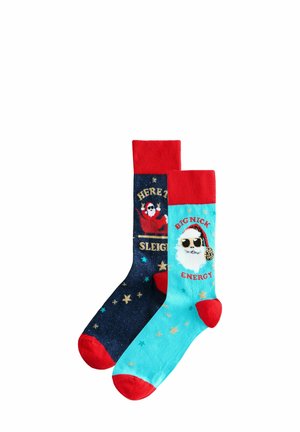 Ein Paar festliche Socken. Eine marineblaue Socke mit roten Bündchen und goldener Schrift; die andere hellblaue Socke mit roten Akzenten und einem Weihnachtsmann-Motiv. Weicher, gemusterter Stoff.