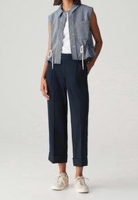 Débardeur cropped sans manches bleu et blanc avec cordon de serrage, associé à un pantalon large marine et des baskets blanches.