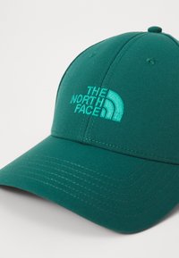 Casquette verte en tissu texturé, ornée d'un logo brodé dans une teinte plus claire. Visière courbée et détails cousus.
