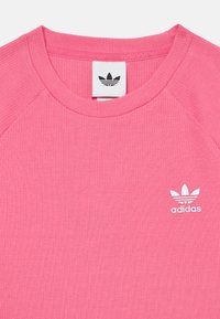 Pink ribbed T-shirt with a crew neck and white Adidas logo on the left chest. Features raglan sleeves for added comfort.