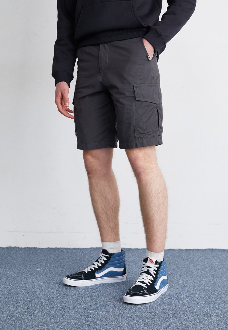 Pantalones cortos de carga grises con bolsillos laterales, textura de la tela visible. Combinados con zapatillas altas en azul marino y azul, con cordones y suela blanca.