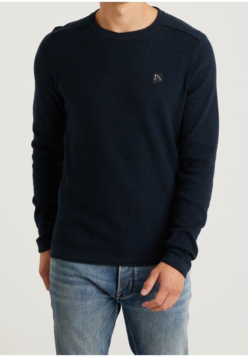 Granatowy sweter z dzianiny z okrągłym dekoltem, długimi rękawami, teksturowanym wzorem i małą naszywką z logo na klatce piersiowej.