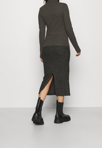 Jupe longue grise avec une fente sur le côté, associée à un haut noir ajusté. La tenue est complétée par des bottes noires à semelle épaisse.