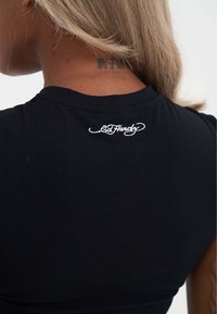 Černé bavlněné tričko s přiléhavým střihem. Na zadní straně límce je bílé vyšívané logo "Ed Hardy". Hladký materiál, krátké rukávy.