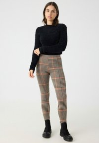 Suéter negro peludo combinado con leggings de cuadros de cintura alta en beige, negro y rojo; modelo vistiendo botas de tobillo gruesas en negro.