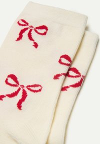 Cremefarvede bomuldsokker med røde båndmotiv, som har en glat tekstur og ribbede manchetter for en tætsiddende pasform.