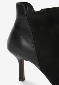 Stivale alla caviglia nero con un design elegante, caratterizzato da una combinazione di pelle liscia e suede, punta affusolata e tacco sottile.
