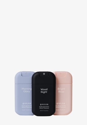 Trzy pojemniki na środek do mycia rąk: jasno-fioletowy, czarny i jasno-różowy. Każdy ma zaokrąglone kształty, klapkę na górze i czytelne etykiety.