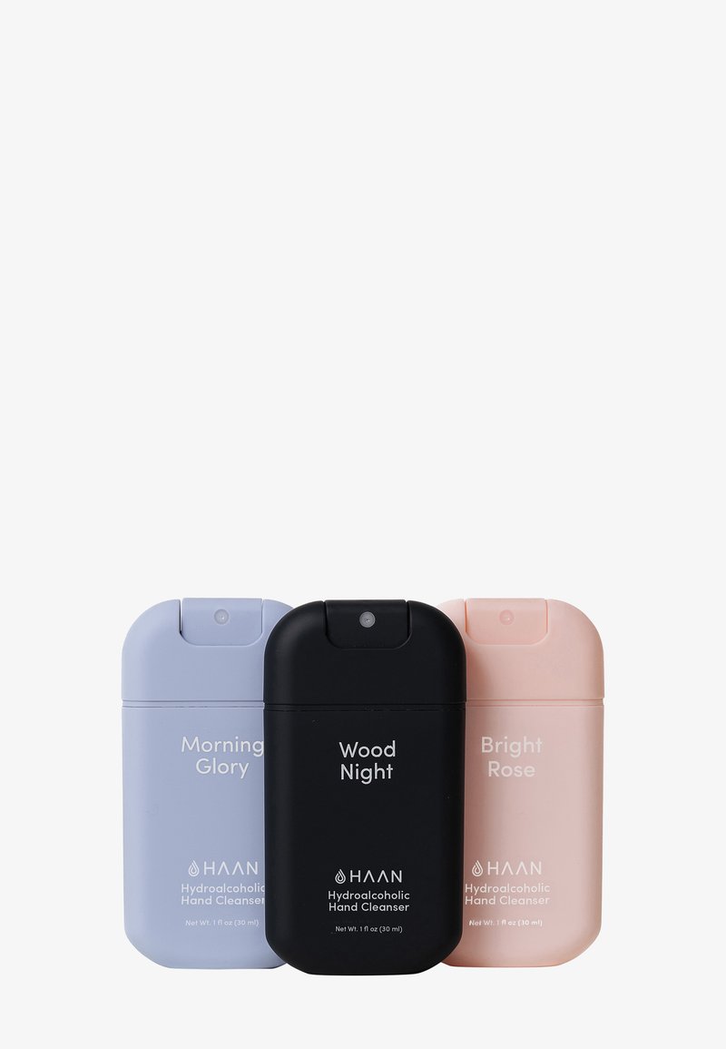 Tres envases de limpiador de manos: púrpura claro, negro y rosa claro. Cada uno presenta formas redondeadas, una tapa de tipo flip-top y etiquetado claro.