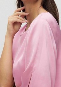 Top in satin rosa chiaro con maniche corte, caratterizzato da una vestibilità rilassata e una delicata lucentezza, che mette in evidenza la texture fluida e il morbido cadere.