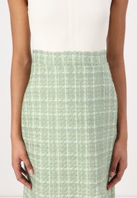 Grønn tweed midi-skjørt med en teksturert overflate, med et rutete mønster og en tettsittende silhuett.