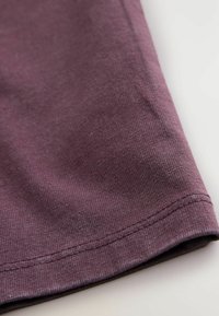 Lähikuvassa violetti puuvillakangas, jossa on ribat textuuri, ommeltu reuna ja sileä pinta, jossa on vaaleita sävyvaihteluita.