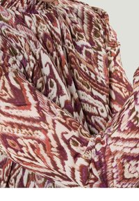 Blouse à manches longues et col montant présentant un motif abstrait tourbillonnant multicolore dans des teintes de rose, bordeaux et crème. Tissu texturé.