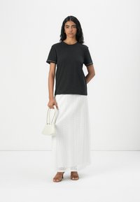 T-shirt en coton noir à manches courtes avec des coutures contrastées, associé à une jupe maxi blanche brodée, un sac à main beige et des sandales brunes à lanières.