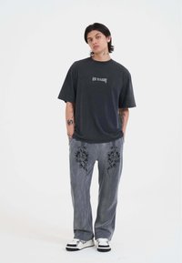 Camiseta negra de gran tamaño con logotipo blanco, combinada con pantalones grises que presentan diseños florales bordados en negro, y zapatillas en blanco y negro.