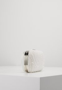Biała kopertówka z perłowymi ozdobami, prostokątny kształt, metalowy zamek, oraz teksturowana powierzchnia. Elegancki i minimalistyczny design.