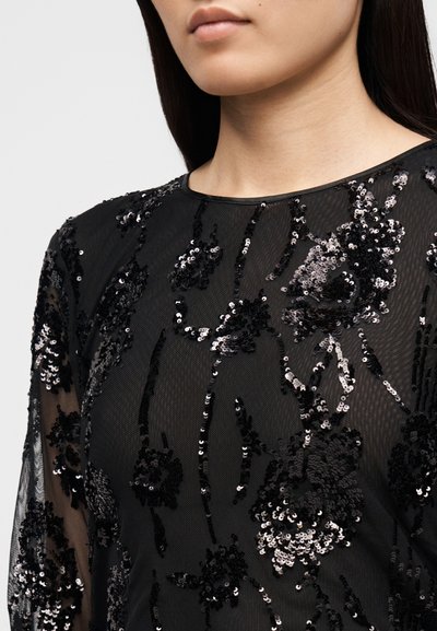 Mustast läbipaistvast kangast kleit, millel on lillemustriline litritega tikand, pikad varrukad ja ümar kaelus, tekstuurse viimistluse ja keerukate detailidega.