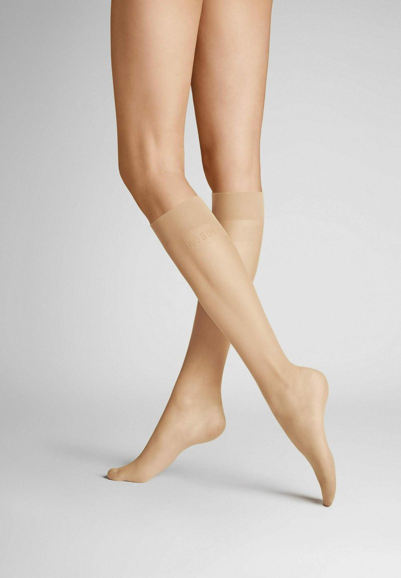 Beige kniehohe Socken mit einer glatten Textur, die ein dezentes Logo am oberen Rand aufweisen. Schlichtes Design, anliegende Form und transparentes Material.