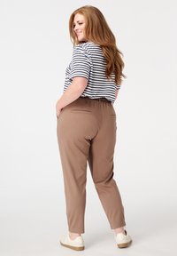 Haut à rayures à manches courtes associé à un pantalon marron fuselé avec une taille élastique et des poches arrière ; porté avec des baskets blanches.