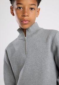 Gray zip-up sweater with a high collar, featuring a soft texture and a front zipper. Designed for a fitted look.