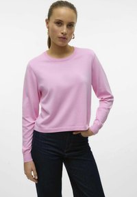 Felpa a maniche lunghe rosa chiaro con scollo rotondo, dal fit rilassato e polsini a costine, abbinata a jeans in denim scuro. Texture liscia.