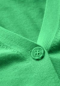 Grön stickad cardigan med en mjuk textur, V-ringad design och en transparent knapp med fyra hål på vänster sida.