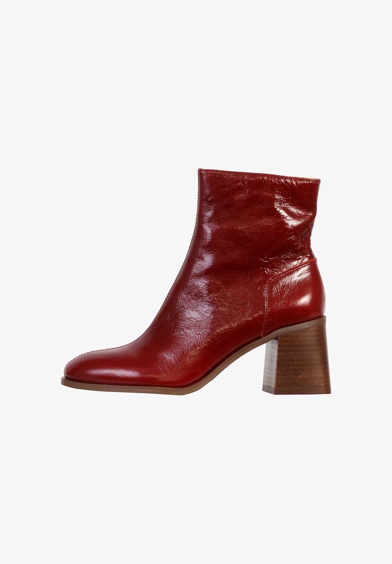 Botín de cuero rojo hasta el tobillo con punta afilada, acabado texturizado y tacón de madera gruesa. Presenta un caña ajustada y un diseño minimalista.
