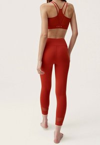 Röd sportbehå med tunna band och en urtagning på baksidan, kombinerad med röda leggings med nätdetaljer vid anklarna. Slät, elastisk material.