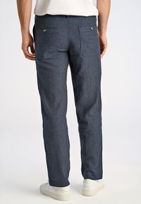 Mörkblå randiga byxor med rak benpassform, två bakfickor och silverknappar, i kombination med vita skor.