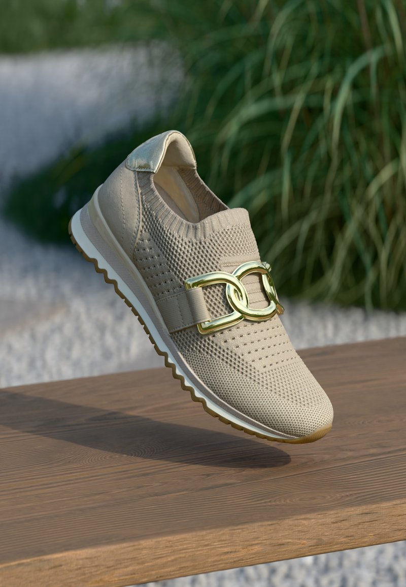 Μπεζ αθλητικό παπούτσι με πλεκτό επάνω μέρος, χρυσή αλυσίδα ως διακοσμητικό στοιχείο και υφή στην επιφάνεια πάνω σε ξύλινη βάση. Εύκαμπτη σόλα από καουτσούκ.