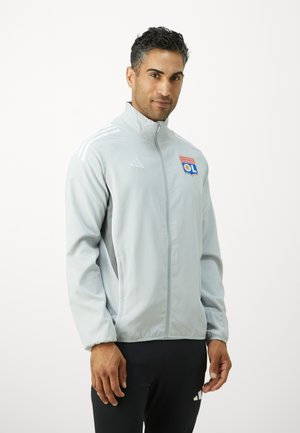 Svetlo siva športna jakna z visokim ovratnikom, z zadrgo in Adidas logotipom. Ima tri bele črte na rokavih in značko ekipe.