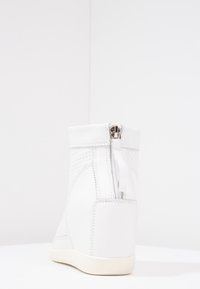 Baskets montantes blanches avec panneaux texturés et fermeture éclair à l'arrière, présentant une finition en cuir lisse et une semelle contrastée.