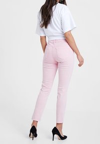 Jeans rosa claro con corte recto, cintura alta y bolsillos traseros; combinados con una camiseta blanca cropped y zapatos de tacón negros.