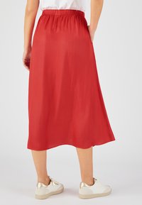 Falda midi roja con cintura elástica y textura suave. Combinada con zapatillas blancas con detalles dorados.