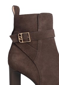 Brown suede ankle boot with a high heel, featuring a buckle strap accent and stitch detailing, smooth texture, and sleek silhouette.