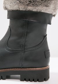 Botte d'hiver en cuir noir avec semelle en caoutchouc épaisse et bord en fausse fourrure grise, coutures détaillées et petit écusson de marque sur le talon.