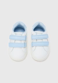 Λευκά παπούτσια μωρού με ανοιχτό γαλάζιο βέλκρο, με την ετικέτα "Tommy Hilfiger", μέγεθος 20, φωτογραφημένα από πάνω σε απλό φόντο.