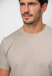 Beige t-shirt med rund hals i mjukt tyg. Lätt textur synlig, kroppsnära design, korta ärmar och inga framträdande logotyper eller mönster.