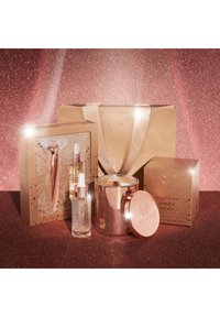 Ein goldenes Geschenkeset umfasst eine kristalline Duftkerze, zwei Serumfläschchen und einen Gesichtsroller, alles mit roségoldenen Akzenten und eleganter Verpackung.
