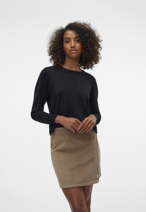 Maglietta nera a maniche lunghe abbinata a una mini gonna in corduroy color beige con uno spacco laterale. La texture del tessuto è liscia per la maglietta e a costine per la gonna.