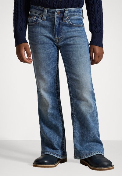 Blå denim flared jeans med ljus tvätt, utrustade med knäppning, fem fickor och synliga sömnadsdetaljer, bärs med svarta träskor.