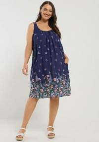 Ärmelloses blaues Kleid mit Blumenmustern, das über ein gerafftes Oberteil, Seitentaschen und einen Saum mit mehrfarbigen Blumen verfügt.