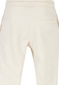 Cremefarvede sweatpants med en glat tekstur, der har en baglomme og en elastisk talje for justerbar pasform.