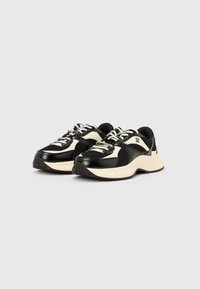 Μαύρα και κρεμ αθλητικά παπούτσια με υλικά από δίχτυ και δέρμα, στρογγυλεμένη μύτη, επίπεδο κλείσιμο με κορδόνια και λαστιχένια σόλα. Διακριτικό λογότυπο στο πλάι.