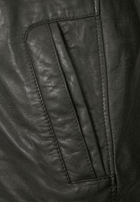 Schwarzer Lederstoff mit einer auffälligen aufgesetzten Tasche und Stichdetails, die eine weiche Textur und ein leicht zerknittertes Aussehen zeigen.