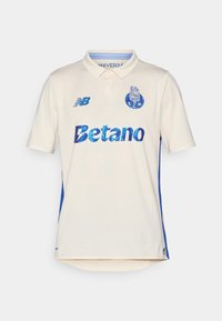 Polo shirt crème avec des panneaux latéraux bleus. Présente le logo "Betano" en bleu, un tissu texturé et un col. Logo New Balance sur la poitrine.