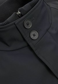 Must värvusega veekindel jakk, millel on püsti kaelus, lukuga sulgemine ja kaks musta nööpi. Silene tekstuur koos soonikdetailidega kaeluses.